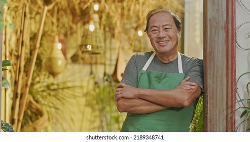 An Asian American Business Owner Wearing Apron And Crossing Arms Smiling. Portrait Of An Asian Middle Aged Businessman Owner Of Small Local Store With Arms Crossed Looking At Camera