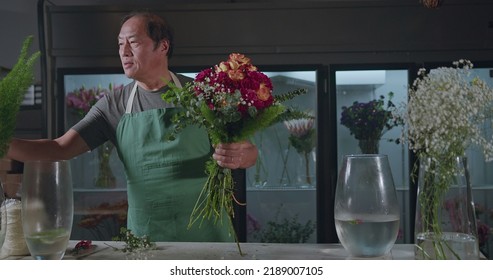 An Asian American Florist Preparing Bouquet Of Flowers For Online Delivery. Portrait Of An Artisan Male Florist Creating Artistic Arrangement For Client At Flower Shop