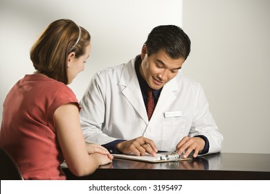 Asian American Male Doctor Consulting With Caucasian Female Patient.