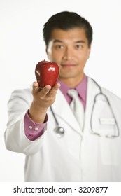 Asian American Male Doctor Holding Out Apple.