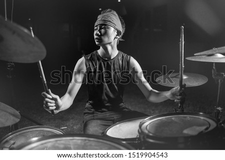 Asian American mixed teenager playing drums at home garden . cool and handsome young boy practicing on drum kit rehearsing passionate in badass rock band look enjoying the practice