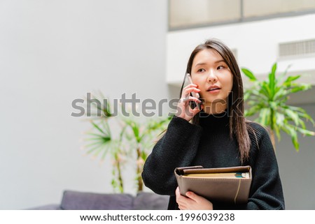 asian american multiracial asian business woman, talking on the phone and holding a notebook in her hands, student indoors. copy space