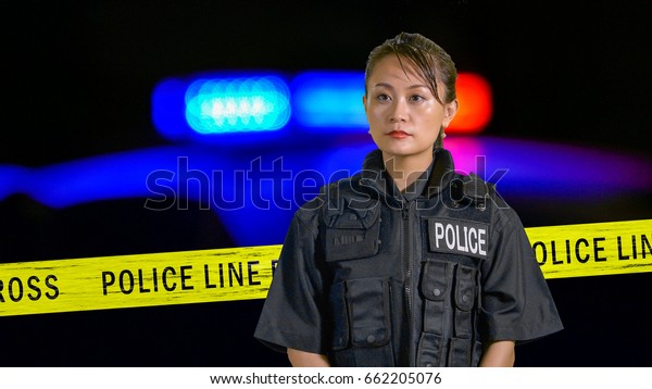 Asian American Policewoman using\
police radio with siren and boundary tape in\
background