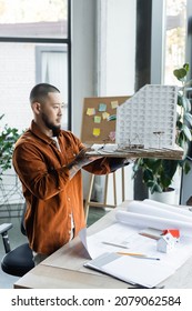 Asian Architect Holding House Model Near Blueprints On Desk In Office