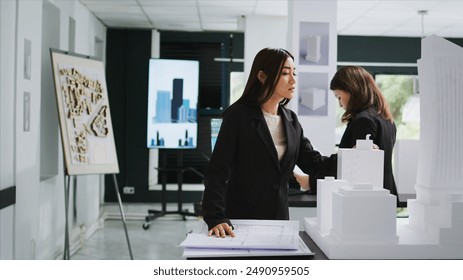 Asian architect studying blueprint papers in creative agency, examining building model on desk. Technician looking at property floor plan to design new home for clients, 3d maquette. - Powered by Shutterstock