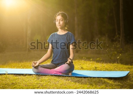 asian athlete women meditating in a zen-like position or padmasana pose while listening to music on a headphone at sunrise