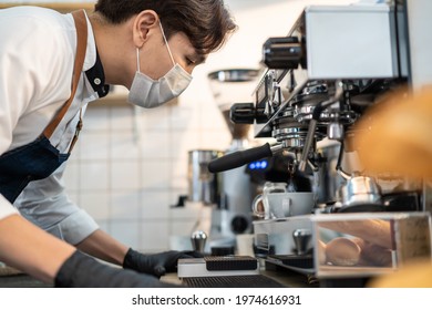 Asian Attractive Cafe Business Owner Man Wear Facemask And Shield Due To Covid 19 Pandemic. Young Expert Barista Or Waiter Look To Grinder Machine While Making Hot Coffee On Counter Bar In Restaurant.