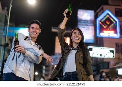 Asian Attractive Couple Drinking Alcohol And Having Party Together. Young Man And Woman Tourist Travel In City Spend Time On Holiday Vacation Together Holding Bottle Of Beer At Dark Night On The Road.