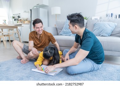 Asian attractive LGBTQ gay family looking young girl kid draw picture  Handsome male couple teaching little cute child daughter painting color book in living room  enjoy parenting activity at home 