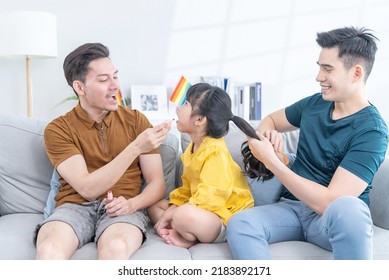 Asian Attractive LGBTQ Gay Family Spending Time With Girl Kid Daughter. Handsome Male Couple Sit On Sofa In Living Room, Take Care And Comb Little Adorable Child Hair Enjoy Parenting Activity At Home.