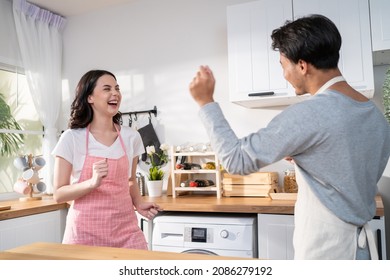 Asian Attractive Loving Couple Enjoy Dance Together In Kitchen At Home. Beautiful Romantic New Marriage Man And Woman Wear Aporn Feeling Happy And Enjoy Activity Relationship In House Listen To Music.