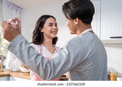 Asian Attractive Loving Couple Enjoy Dance Together In Kitchen At Home. Beautiful Romantic New Marriage Man And Woman Wear Aporn Feeling Happy And Enjoy Activity Relationship In House Listen To Music.