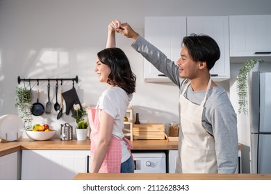 Asian Attractive Loving Couple Enjoy Dance Together In Kitchen At Home. Beautiful Romantic New Marriage Man And Woman Wear Aporn Feeling Happy And Enjoy Activity Relationship In House Listen To Music.