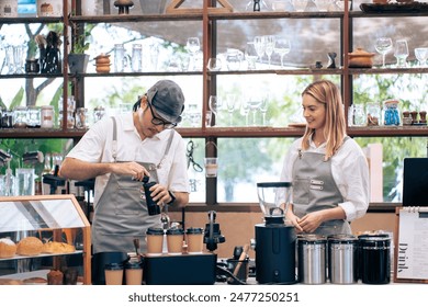 Asian attractive male barista or waiter working in coffeehouse shop. Young handsome entrepreneur man in apron teaching waitress grinding roasted beans making coffee on counter at urban restaurant cafe - Powered by Shutterstock