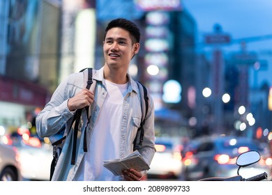 Asian attractive man backpacker walking around the city at night road. Young handsome guy tourist traveler travel alone on street use map to find destination, enjoy spend time on holiday vacation trip - Shutterstock ID 2089899733