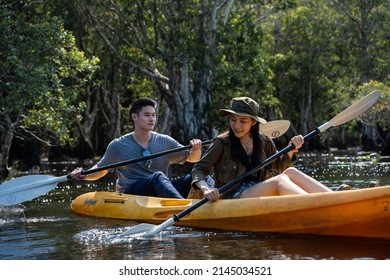 Asian attractive romantic young couple rowing kayak in a forest lake. Backpacker man and woman travel and kayaking on canoe in beautiful mangrove forest enjoy spend time on holiday vacation together.