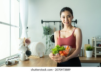 Asian attractive sport woman holding salad bowl and eat vegetables. Beautiful sport girl in sportswear enjoy eat clean vegetables after exercise for health in house. Diet and Healthy food concept. - Shutterstock ID 2070973889