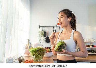 Asian attractive sport woman holding salad bowl and eat vegetables. Beautiful sport girl in sportswear enjoy eat clean vegetables after exercise for health in house. Diet and Healthy food concept. - Shutterstock ID 2140016177