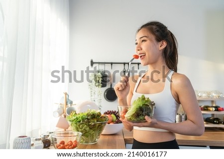 Asian attractive sport woman holding salad bowl and eat vegetables. Beautiful sport girl in sportswear enjoy eat clean vegetables after exercise for health in house. Diet and Healthy food concept. Сток-фото © 