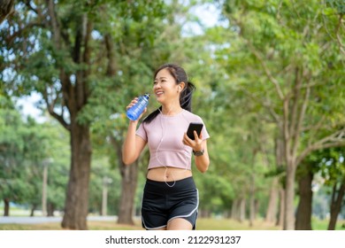 Asian Attractive Sporty Woman Drinking Water From A Bottle After Jogging Or Running While She Sitting In Park.