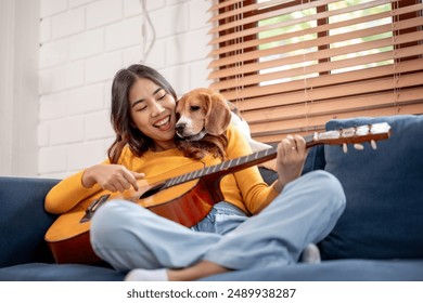 Asian attractive woman play with her beagle dog in living room at home. Young female owner feeling happy and relax, enjoy play guitar and spend leisure time with her lovely pet puppy together in house - Powered by Shutterstock