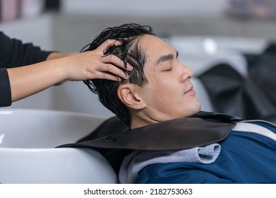 Asian Attractive Young Male Get Hair Washed By Hairdresser In Salon. Professional Hair Stylist Woman Give Service And Hair Wash And Massage To Handsome Man Customer Lying Down On Salon Washing Bed.