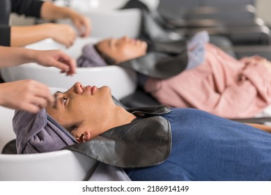 Asian Attractive Young Male Get Hair Washed By Hairdresser In Salon. Professional Hair Stylist Woman Give Service And Hair Wash And Massage To Handsome Man Customer Lying Down On Salon Washing Bed.