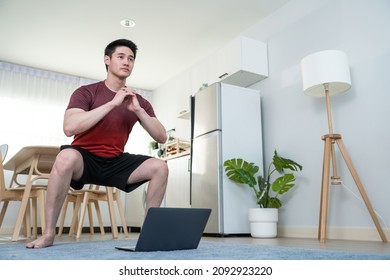 Asian Attractive Young Man Doing Exercise Using Laptop In Living Room. Handsome Male In Sport Cloth Follow Exercise Or Yoga Instruction Video Online Trainer Workout At Home. Healthy Lifestyle Concept.