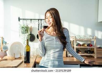 Asian Attractive Young Woman Drinking Wine In Glass In Kitchen At Home. Beautiful Girl Feel Happy While Stand Alone And Enjoying Celebrate Life Moving To New House. Leisure Activity On Weekend Concept