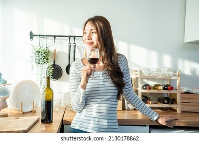 Asian Attractive Young Woman Drinking Wine In Glass In Kitchen At Home. Beautiful Girl Feel Happy While Stand Alone And Enjoying Celebrate Life Moving To New House. Leisure Activity On Weekend Concept