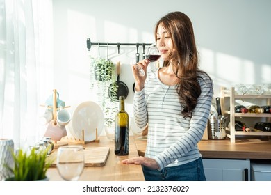 Asian Attractive Young Woman Drinking Wine In Glass In Kitchen At Home. Beautiful Girl Feel Happy While Stand Alone And Enjoying Celebrate Life Moving To New House. Leisure Activity On Weekend Concept