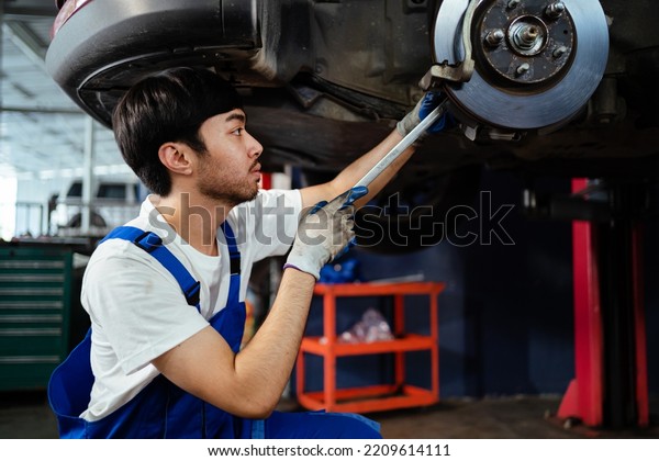 Asian auto mechanic in car garage. Vehicle service\
personnel are inspecting cars in mechanic factory with confidence\
in car engine repairs. Asian mechanic with equipment to fix cars in\
the service. 