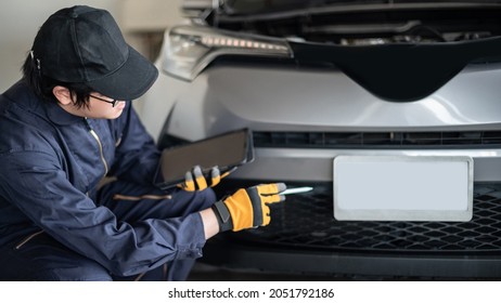 Asian auto mechanic holding digital tablet checking car engine and license plate in auto service garage. Mechanical maintenance engineer working in automotive industry. Automobile servicing and repair
