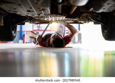 Asian auto mechanic sleeps under the car to Check the car suspension with rebar during balance adjustment. Align the car suspension at the auto repair station.