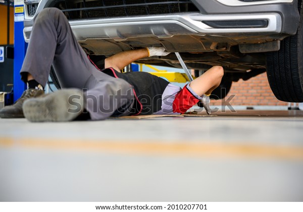 Asian auto mechanic sleeps under the\
car to Check the car suspension with rebar during balance\
adjustment. Align the car suspension at the auto repair\
station.