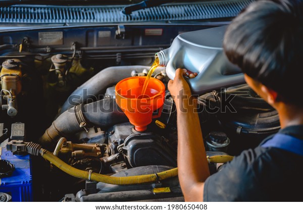 Asian auto mechanic works in auto repair\
shops. Pour the engine oil to change the engine oil in the garage\
for customers who do car repair and oil\
change.