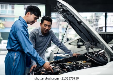 Asian automotive mechanic explain car condition to client in garage. Vehicle service manager male work in mechanics workshop point at vehicle part to customer man for maintenance and repair car engine - Shutterstock ID 2132375959