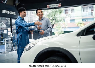 Asian Automotive Mechanic Explain Car Condition To Client In Garage. Vehicle Service Manager Male Work In Mechanics Workshop Point At Vehicle Part To Customer Man For Maintenance And Repair Car Engine