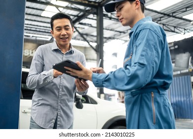 Asian Automotive Mechanic Explain Car Condition To Client In Garage. Vehicle Service Manager Male Work In Mechanics Workshop Point At Vehicle Part To Customer Man For Maintenance And Repair Car Engine