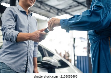 Asian automotive mechanic repairman handing car remote key to client. Vehicle service manager give the key back to car owner after successful of checking and maintenance car engine in mechanics garage - Shutterstock ID 2138052493