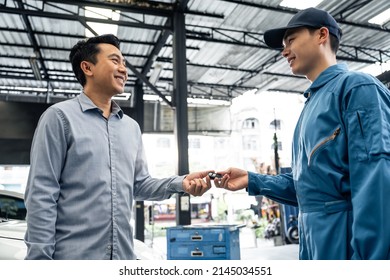 Asian Automotive Mechanic Repairman Handing Car Remote Key To Client. Vehicle Service Manager Give The Key Back To Car Owner After Successful Of Checking And Maintenance Car Engine In Mechanics Garage