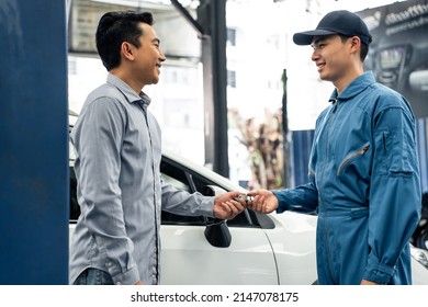 Asian automotive mechanic repairman handing car remote key to client. Vehicle service manager give the key back to car owner after successful of checking and maintenance car engine in mechanics garage
