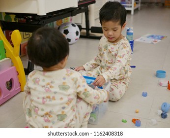 Asian Baby, 31 Months Old, (right) Is Cleaning Up / Putting Away Toys She Played With Her Little Sister