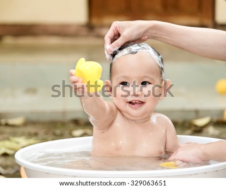 Asian baby boy outdoor bathing in the white bathtub . He is smiling and playing yellow duck full of happiness, Country side culture of Thailand 