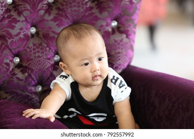 An Asian Baby Boy Sitting On The Purple Velvet Couch.