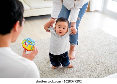 Asian Baby Boy Toddler Taking First Steps. Family Of Father And Mother Encouraging Their Son Learning To Walk At Home