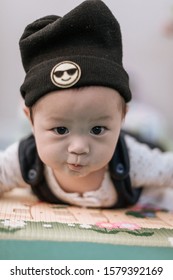 Asian Baby Boy Wearing Black Knitted Beanie Lying On Play Mat During Tummy Time At Home. Child Is 6 Months Old.