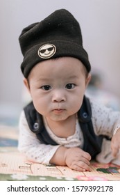 Asian Baby Boy Wearing Black Knitted Beanie Lying On Play Mat During Tummy Time At Home. Child Is 6 Months Old.