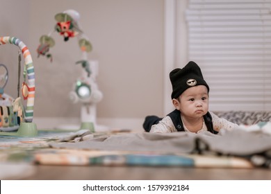 Asian Baby Boy Wearing Black Knitted Beanie Lying On Play Mat During Tummy Time At Home. Child Is 6 Months Old.