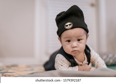 Asian baby boy wearing black knitted beanie lying on play mat during tummy time at home. Child is 6 months old.